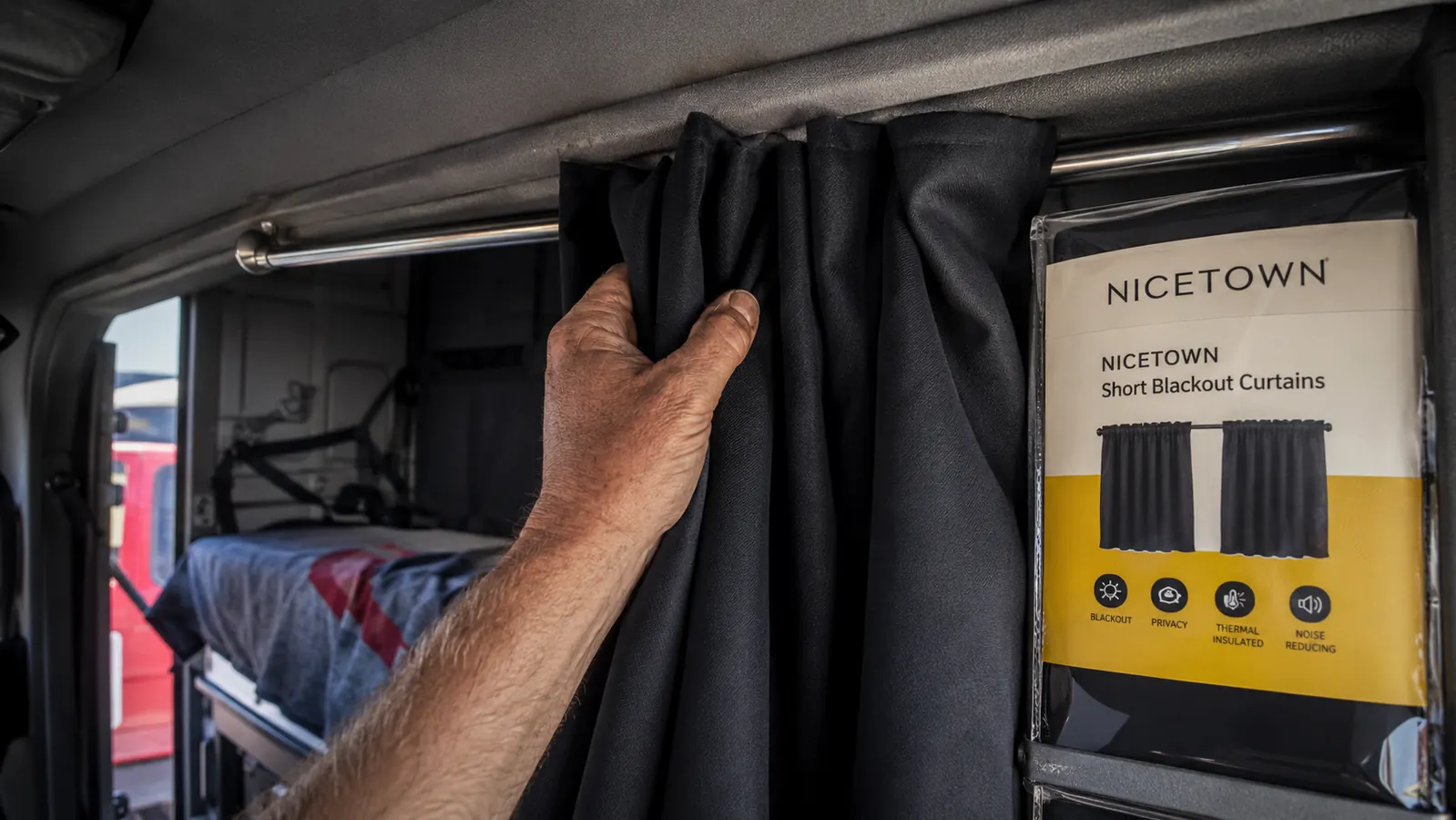 Hand pulling closed a set of dark gray blackout curtain panels across a sleeper bunk window